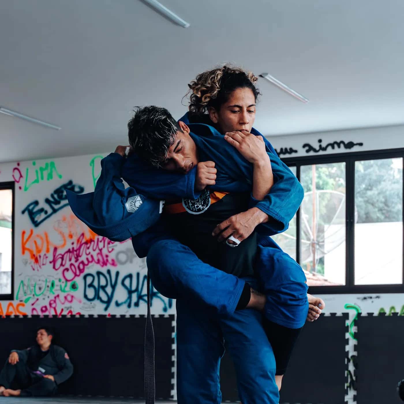 Dois atletas de kimono azul em uma queda durante o treino de competição